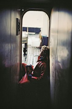 a person sitting on a door way with a red bag in their lap and headphones to their ears