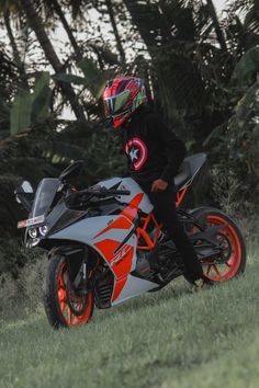 a man riding on the back of a motorcycle down a lush green field next to trees