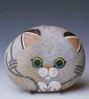 a painted rock with a cat on it's face and green eyes, sitting in front of a gray background