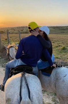 a man and woman riding on the back of white horses in an open field at sunset