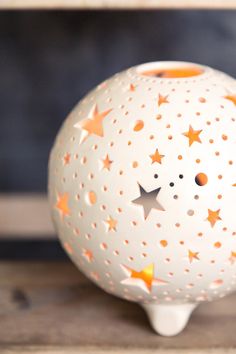 a white ceramic vase with orange and silver stars on the top, sitting on a wooden table