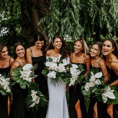 a group of women standing next to each other in front of a tree holding bouquets