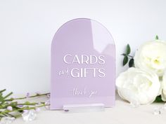 there is a purple card holder with cards and gifts on it next to white flowers