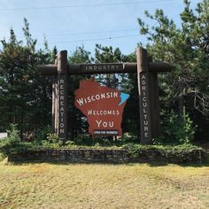 a sign that says wisconsin welcomes you in front of some trees and bushes on a sunny day