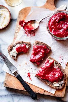 slices of bread with red spread on them next to a jar of cream cheese and spoon