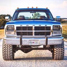 a blue pick up truck parked on top of a gravel road next to a field