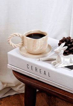 a cup of coffee sitting on top of a white book next to a pine cone