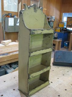 an old green bookcase sitting on top of a workbench in a shop