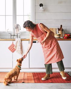 a woman in an orange and white striped apron petting a dog on the nose