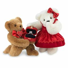 two teddy bears dressed in red and white, one holding a ring box with a diamond on it