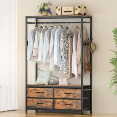 an open closet with clothes hanging on the rack and drawers below it, next to a potted plant