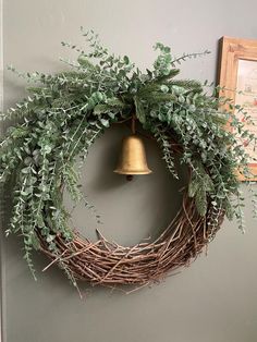 a wreath hanging on the wall with a bell in front of it and greenery