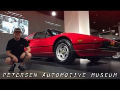 a man kneeling down next to a red sports car on display at an auto museum