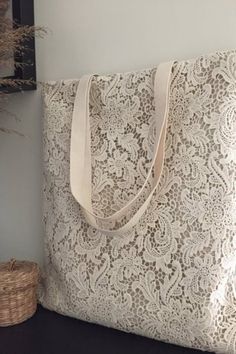 a white lace tote bag sitting on top of a wooden table next to a basket