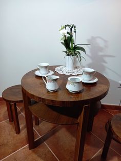 a wooden table topped with white cups and saucers next to a vase filled with flowers