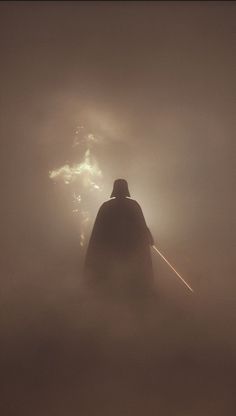 a man with a hat and cape standing in the fog on top of a hill