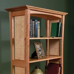 a wooden book shelf with books on top and two vases next to it in front of a green wall