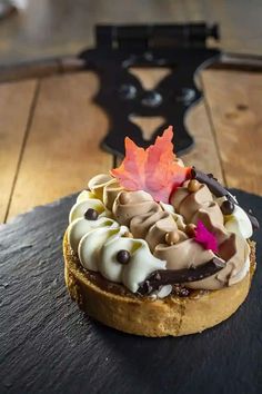 a pastry topped with chocolate, cream and an orange leaf on top of a wooden table