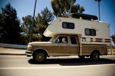 an old truck with a camper on the back is driving down the street in front of palm trees