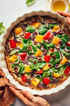 a person holding a pizza with olives, peppers and other toppings in a pie pan