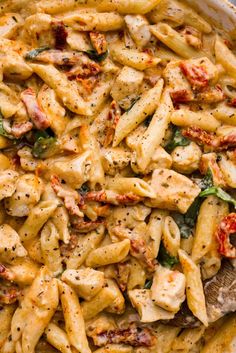 pasta with chicken, spinach and tomatoes in a white dish on a wooden table