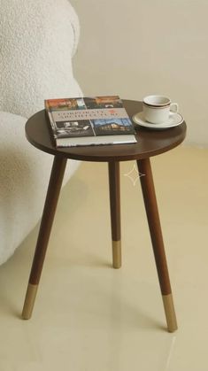 a small table with a magazine on it next to a white chair and a coffee cup