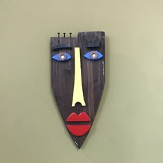 a wooden mask hanging on the wall with blue eyes and red lipstick painted on it