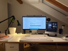 a desk with two computers on it in an attic office space that is also used as a workspace