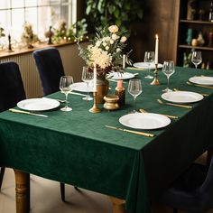 a green table cloth with white plates and wine glasses on it in front of a window