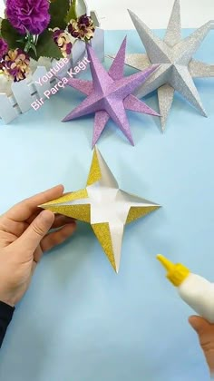 someone is cutting out some paper stars on a blue table with flowers in the background