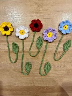 four crocheted flowers on a wooden surface with one flower in the middle and three petals at the end