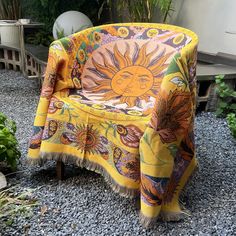 a chair covered in a yellow blanket sitting on top of a gravel ground next to plants