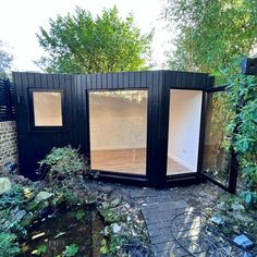 a small black building sitting in the middle of a yard with lots of plants and trees