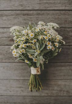 a bouquet of daisies and greenery tied to a wooden wall with the stems still attached