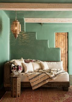 a bed with pillows and blankets on top of it in front of a green wall