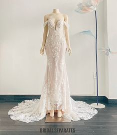 a wedding dress on display in front of a white wall and blue flower behind the mannequin