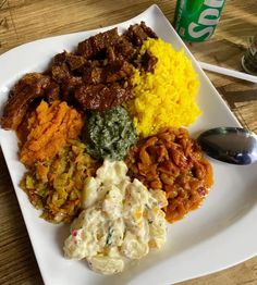 a white plate topped with different types of food next to a can of soda on top of a wooden table