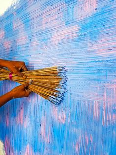 a woman is painting the wall with blue and pink paint, holding a bundle of straws