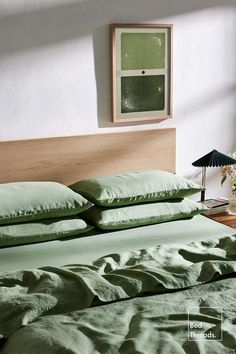 a bed with green sheets and pillows in a room next to a lamp on a table