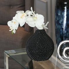 a black vase with white flowers in it on a glass table next to a brown chair