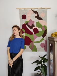 a woman standing in front of a wall hanging on the wall next to a plant