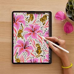 a woman's hand holding a pencil and drawing on an ipad with pink flowers