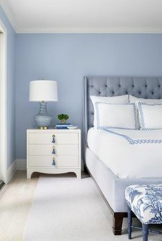 a bedroom with blue walls, white bedding and an upholstered footstool