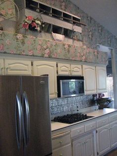 a kitchen with white cabinets and floral wallpaper on the walls, along with a silver refrigerator freezer