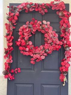 a wreath made out of red flowers and pine cones is hanging on the front door