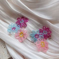 two pairs of colorful beaded flower earrings on a white fabric background with pearl beads