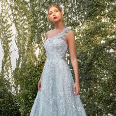 a woman in a blue dress standing next to some bushes