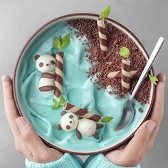 someone is holding a bowl filled with blue cake and panda bears on top of it