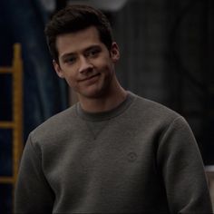 a young man in a grey sweater is looking at the camera while standing with his hands on his hips