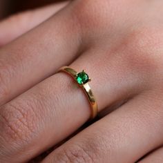 a woman's hand with a gold ring and green gems on it, showing the middle finger